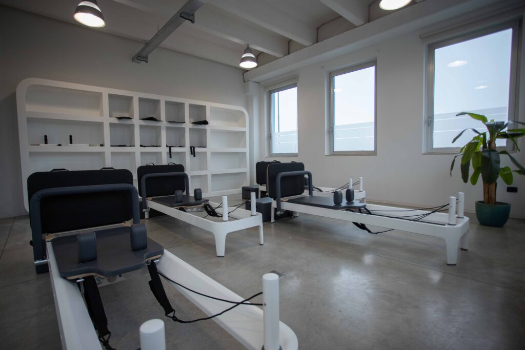 La sala pilates di AXA Studio a Flero: quattro reformer allineati sotto le finestre, pavimento in cemento.