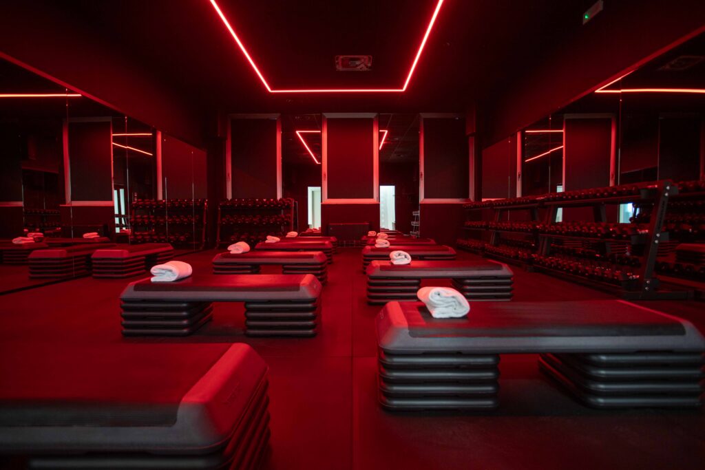 La sala bootcamp di AXA Studio, illuminata dalle linee di neon rosso a soffitto, con step e rastrelliere di manubri.